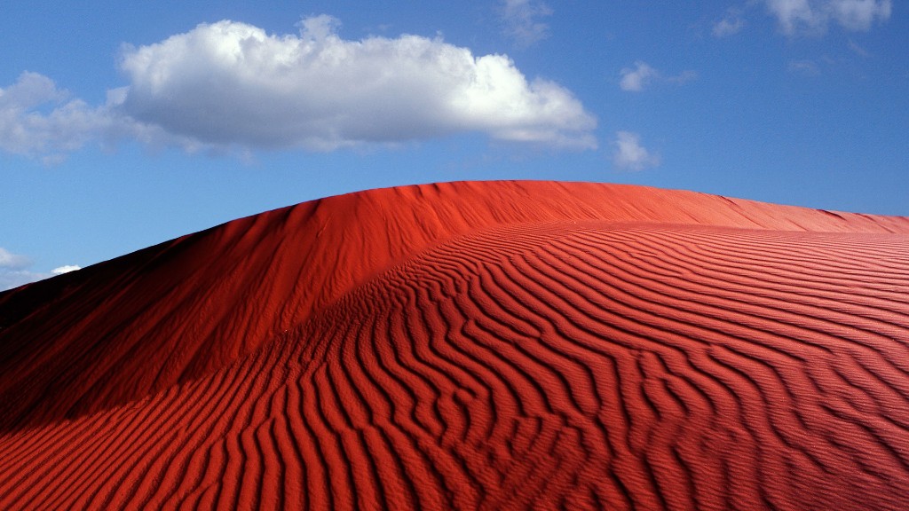 Vibrant red sand dune under a blue sky with a white cloud